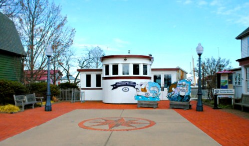 A colorful building with a circular design, surrounded by benches and decorative murals, set in a brick-paved area.
