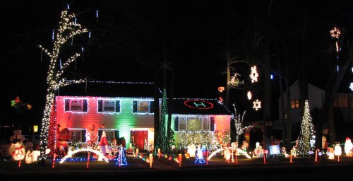 A brightly lit house decorated with colorful Christmas lights, featuring festive displays and decorations in the yard.