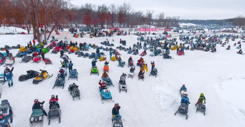 Aerial view of a snowy landscape filled with numerous snowmobiles and people enjoying winter activities.