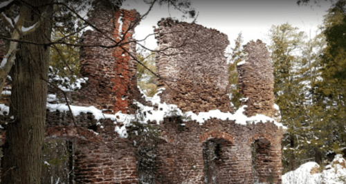 Snow-covered ruins of a stone structure surrounded by trees in a winter landscape.
