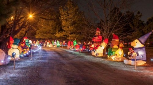 A festive pathway lined with colorful inflatable holiday decorations, including snowmen and teddy bears, illuminated at night.