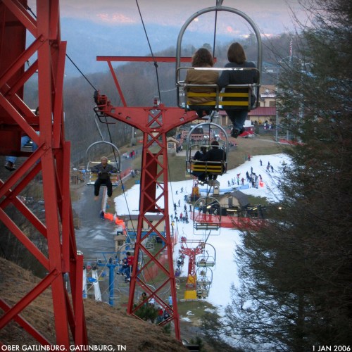 Two people ride a ski lift overlooking a snowy slope and ski resort in Gatlinburg, TN.
