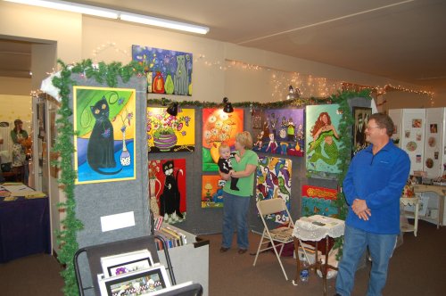 A colorful art exhibit featuring various paintings, with visitors admiring the artwork in a festive setting.
