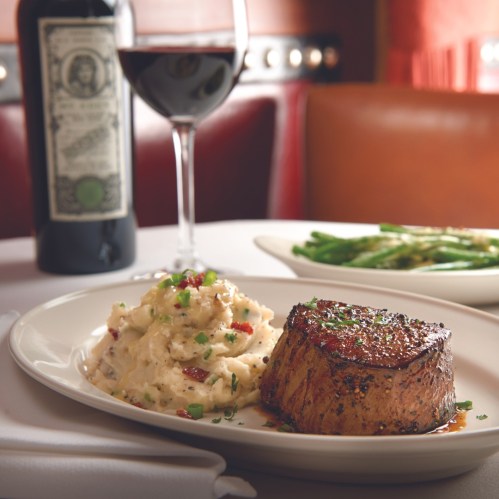 A plate with a grilled steak, creamy mashed potatoes, and green beans, accompanied by a glass of red wine.