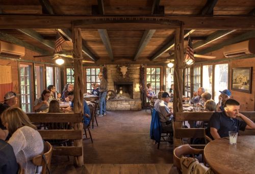 Cozy restaurant interior with wooden decor, a fireplace, and diners enjoying meals at tables.