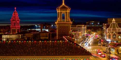 Cityscape at night adorned with colorful holiday lights, featuring illuminated towers and bustling streets.