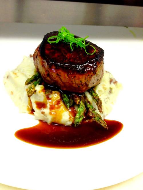A gourmet dish featuring a seared filet mignon atop creamy mashed potatoes, garnished with asparagus and a rich sauce.
