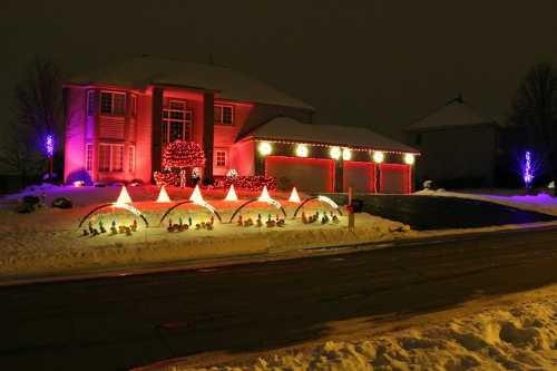 A house decorated with colorful Christmas lights and festive displays in a snowy landscape at night.