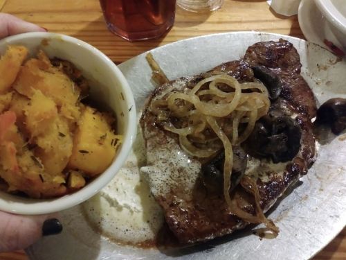 A plate with a grilled steak topped with onions and mushrooms, alongside a bowl of seasoned squash.