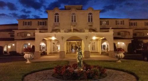 A grand building at dusk, featuring a central statue and landscaped gardens, illuminated by soft lights.