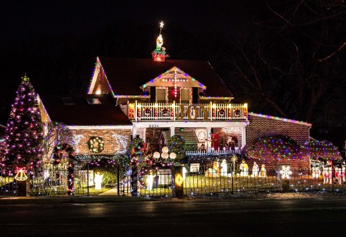A brightly lit house decorated with colorful Christmas lights, featuring a tree and festive decorations in the yard.