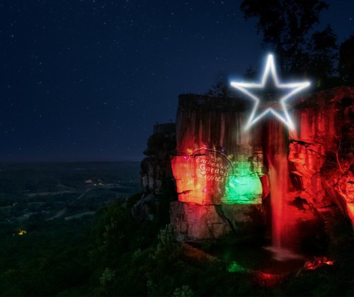 A waterfall illuminated with red and green lights at night, featuring a glowing star above it against a starry sky.