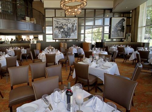 Elegant restaurant interior with neatly set tables, chairs, and large artwork on the walls. Soft lighting creates a warm ambiance.