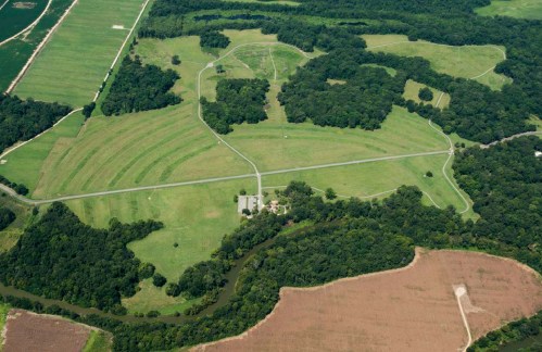Aerial view of a large green landscape with winding roads, fields, and a river running through wooded areas.