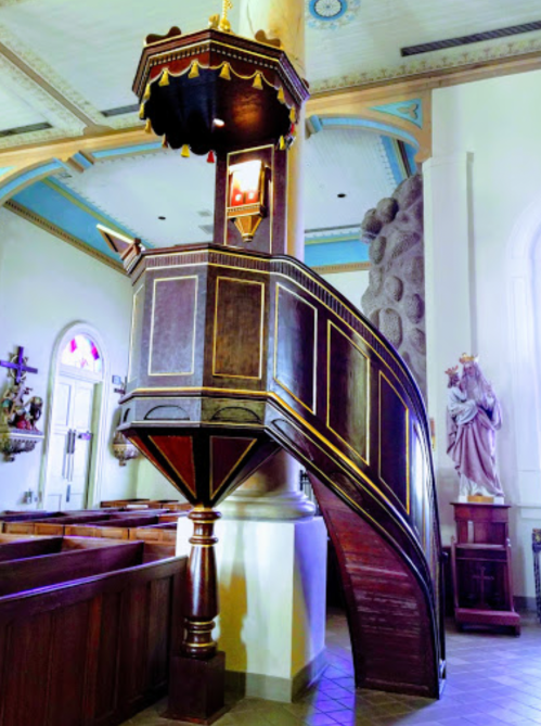 A wooden pulpit with ornate details, situated in a church, featuring a curved design and decorative elements.
