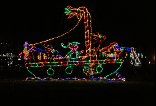 A colorful light display of a boat with festive decorations and characters, set against a dark night sky.