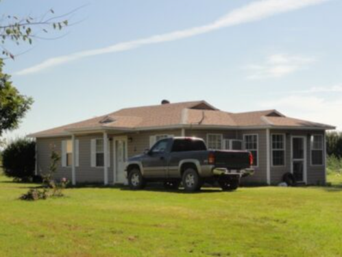 A single-story house with a truck parked in front, surrounded by a grassy yard and clear blue sky.