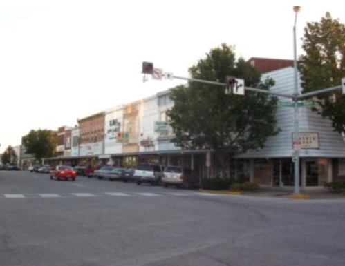 A street view of a small town with shops, parked cars, and traffic lights during sunset.