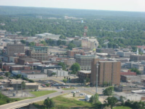 Aerial view of a cityscape featuring buildings, roads, and greenery in the background on a clear day.