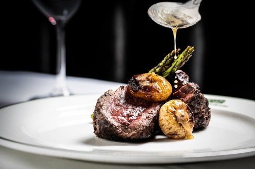 A gourmet plate featuring tender beef, roasted onions, and asparagus, with sauce being drizzled on top.