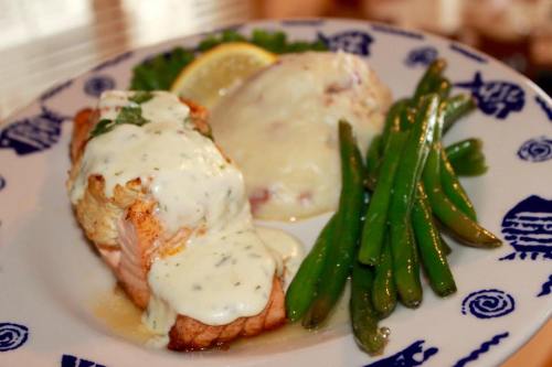 A plate featuring salmon with creamy sauce, mashed potatoes, and green beans, garnished with a lemon slice.