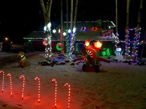 A festive house decorated with colorful lights, candy canes, and holiday figures in a snowy landscape.