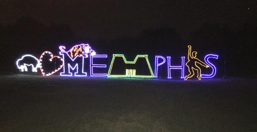 Colorful lights spell out "I ❤️ MEMPHIS" with a bull and a dancer, set against a dark night sky.