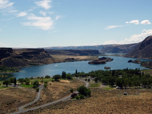 A scenic view of a river winding through arid hills, with greenery and a small settlement along the banks.
