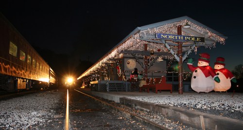 A festive train station decorated for the holidays, featuring snowman decorations and twinkling lights at dusk.