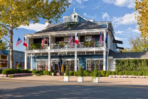 A charming blue building with American and Texas flags, surrounded by greenery and flowers on a sunny day.