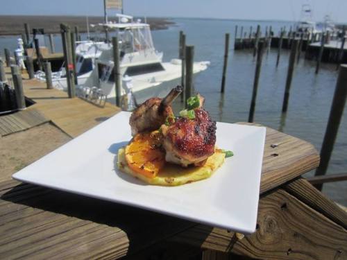 Grilled chicken on a bed of grilled pineapple, served on a white plate with a marina in the background.