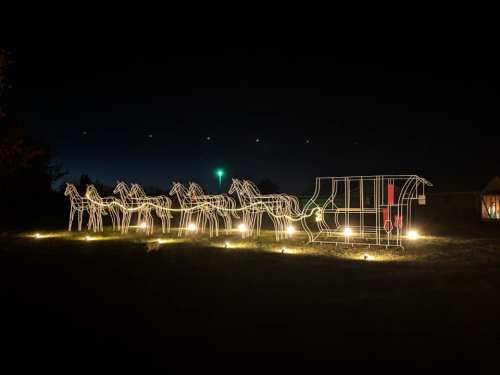 A festive display of illuminated horses pulling a sleigh, set against a dark night sky.