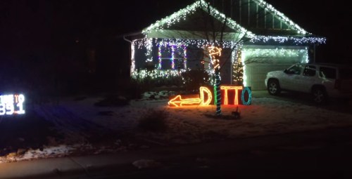 A house decorated with colorful holiday lights, featuring a sign that says "DITTO" and a snowy yard.