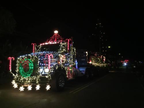 A brightly lit truck decorated with colorful Christmas lights, driving down a dark street during a festive parade.