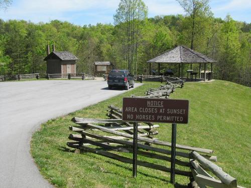 A parking area with a sign stating "Area closes at sunset, no horses permitted," surrounded by greenery and a gazebo.