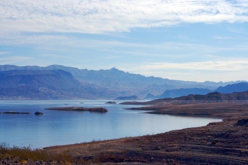 A serene landscape featuring a calm lake surrounded by mountains and islands under a clear blue sky.