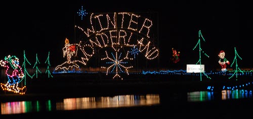 Colorful holiday lights spell "Winter Wonderland," featuring trees, snowflakes, and festive characters by a dark water backdrop.