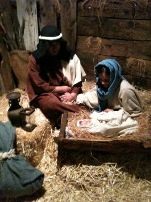 Nativity scene depicting Mary and Joseph with baby Jesus in a manger, surrounded by straw and rustic elements.