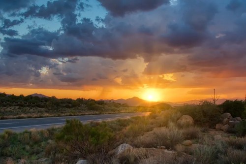 A scenic sunset over a highway, with vibrant clouds and mountains in the background, casting warm golden light.