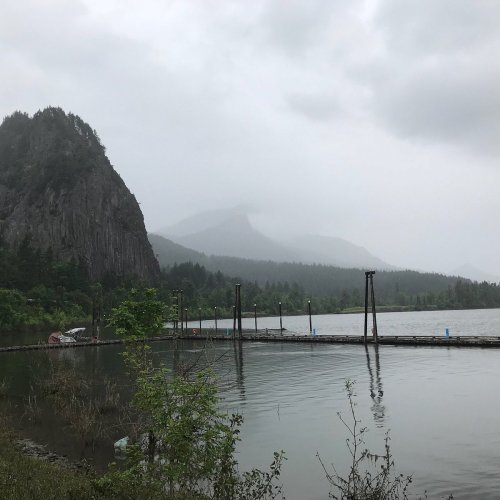 A serene lake surrounded by misty mountains and lush greenery, with a wooden pier extending into the water.