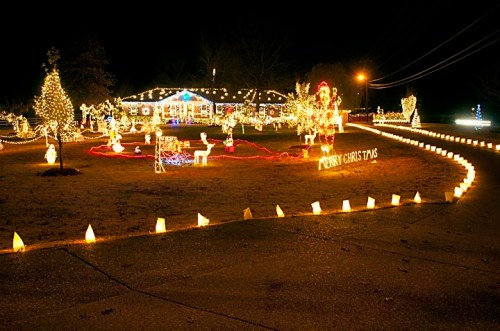 A festive yard decorated with colorful Christmas lights, featuring a "Merry Christmas" sign and illuminated figures.
