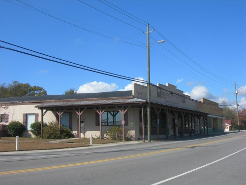 A low-rise building with a covered porch, set along a quiet street under a clear blue sky.