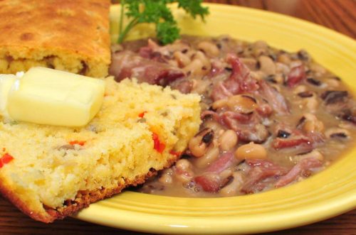 A plate featuring cornbread with butter and a serving of black-eyed peas with ham, garnished with parsley.