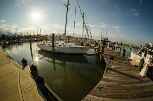 A marina at sunset with sailboats docked and reflections in the water, surrounded by wooden piers.