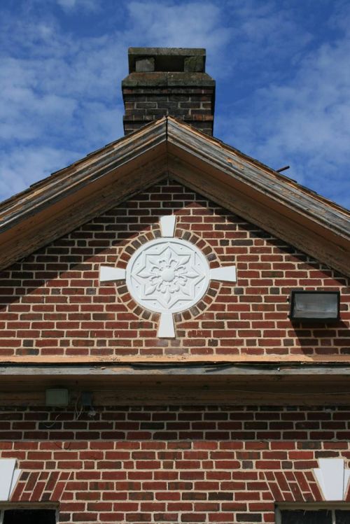 Close-up of a brick building's gable featuring a decorative white emblem against a blue sky.
