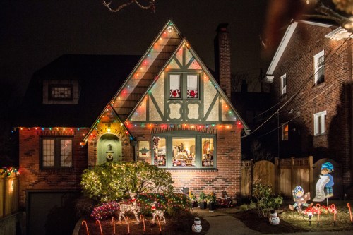 A cozy house decorated with colorful Christmas lights and festive lawn ornaments, glowing warmly at night.
