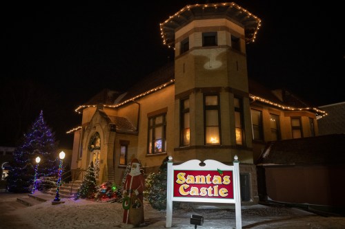 A festive building at night, adorned with lights, featuring a sign that reads "Santa's Castle" and decorated trees.