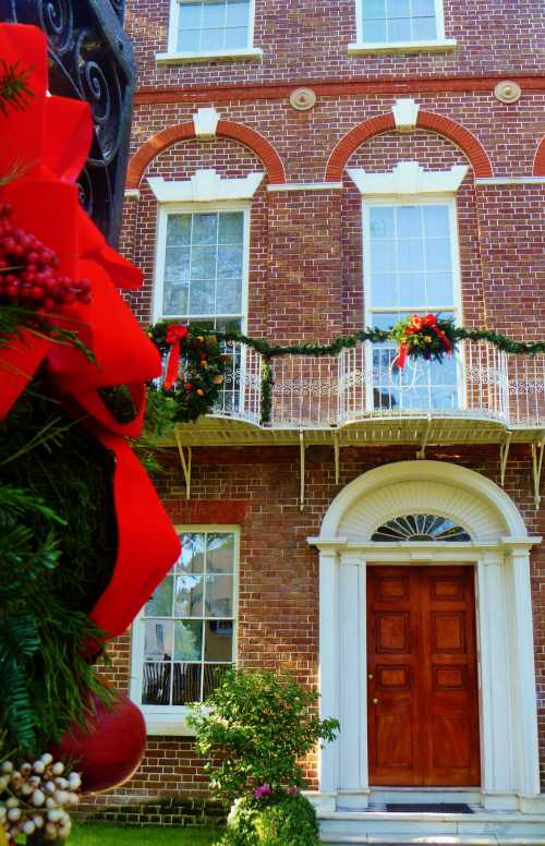 A brick building decorated for the holidays, featuring a large wooden door and festive greenery with red bows.