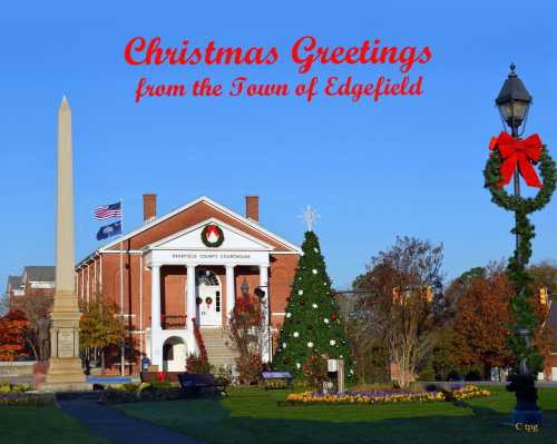 A festive scene featuring a decorated Christmas tree, a monument, and a building with holiday decorations in Edgfield.