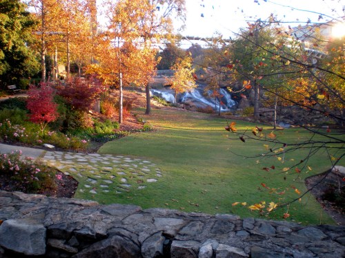 A serene park scene with colorful autumn trees, a grassy area, and a waterfall in the background.